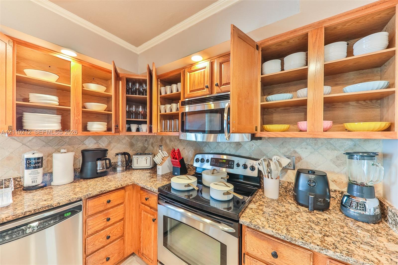 Kitchen featuring wood cabinetry, stone countertops, stone tile backsplash, stainless steel microwave, and stainless steel dishwasher