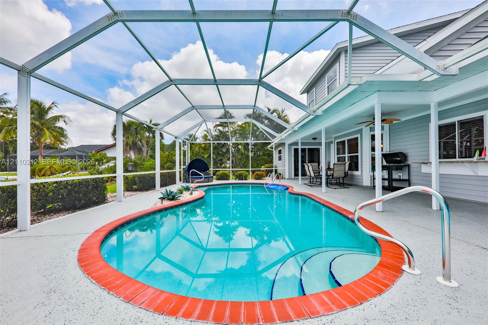 Screen-enclosed swimming pool featuring a brick-accented border, concrete deck, integrated steps, and covered patio area