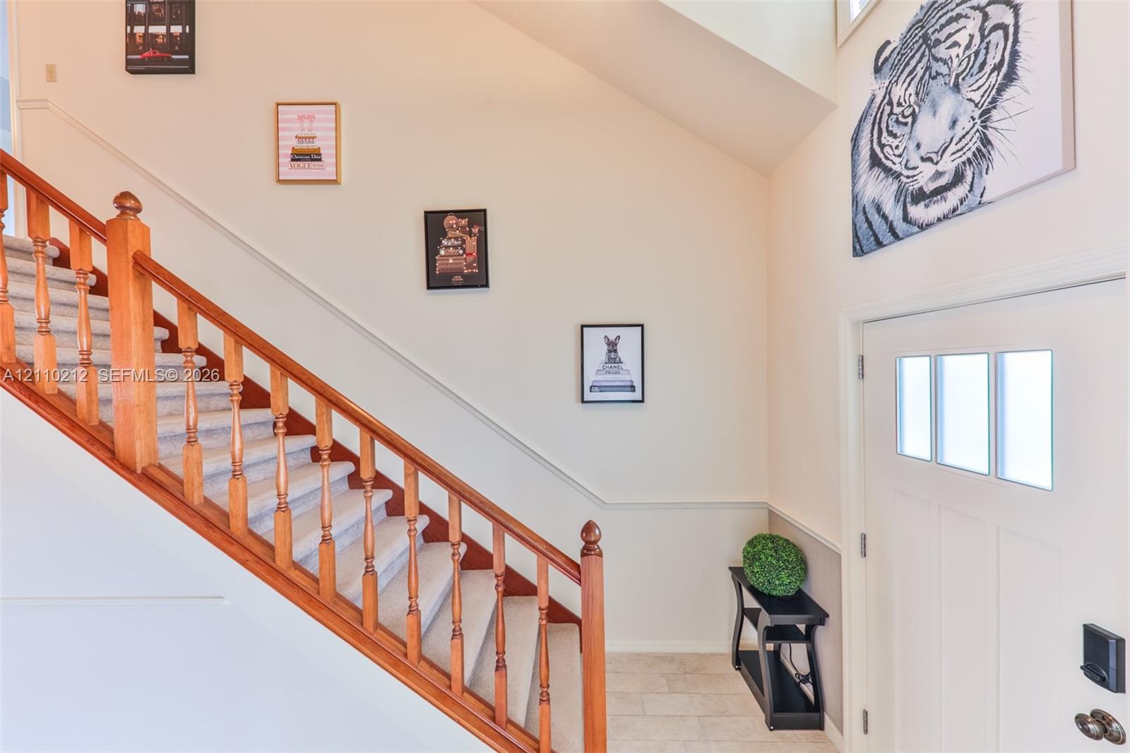 Entryway featuring a staircase with wood railings and balusters, carpeted treads, high ceilings, stone-finish flooring, and a white entry door with a three-pane window