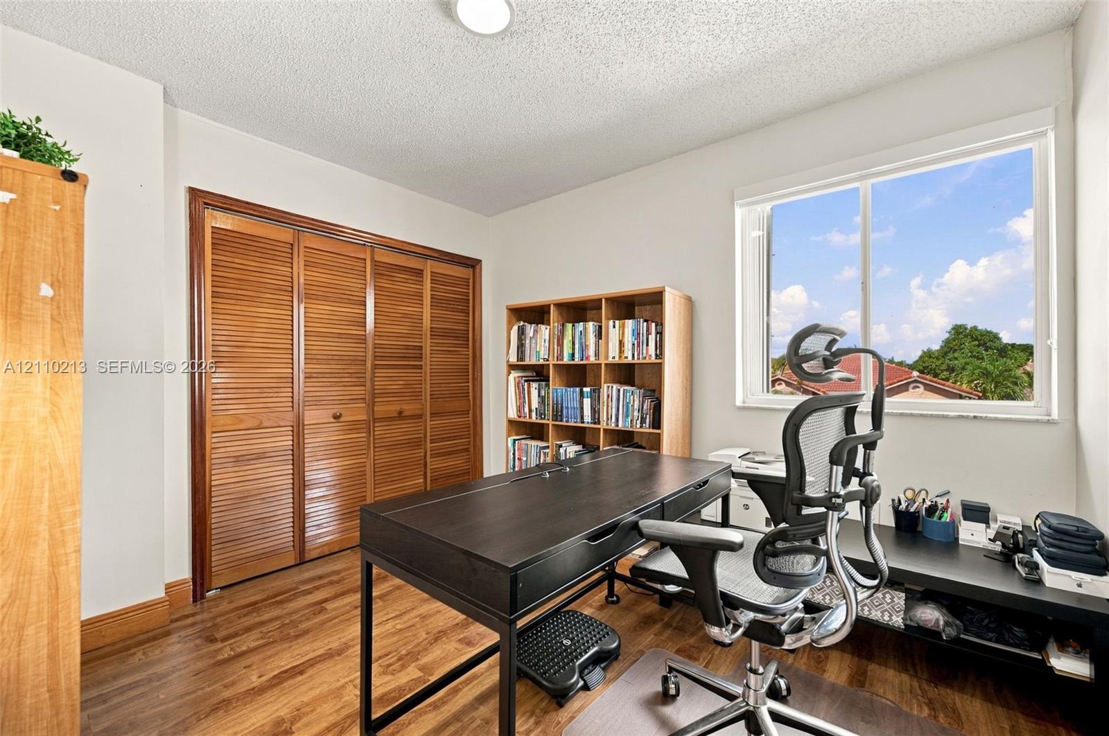 Wood-finish flooring, louvered-style bi-fold closet doors, and large dual-pane window with natural light