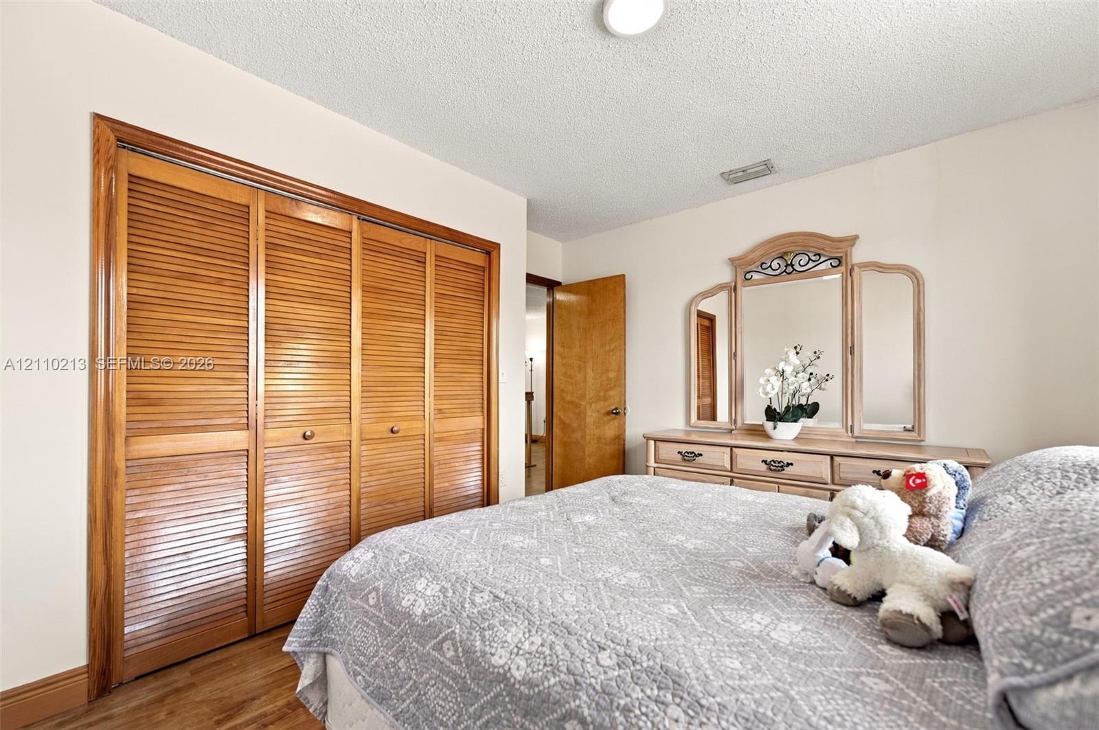 Bedroom featuring wood-finish flooring, four-panel wooden louvered closet doors, and a solid wood interior door