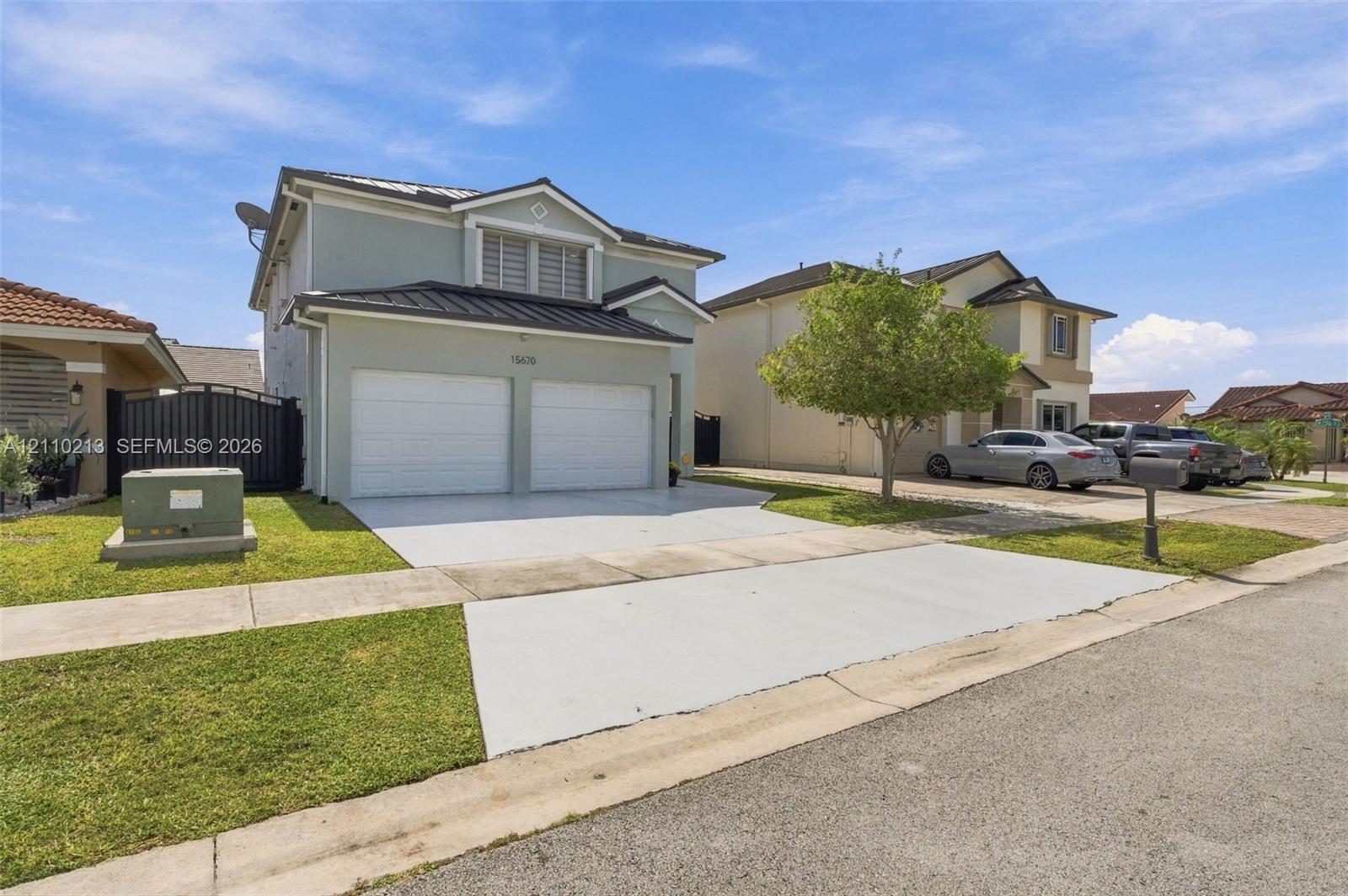 Two-story exterior featuring light-toned stucco siding, a dual-bay garage, a pitched roof, and a concrete driveway