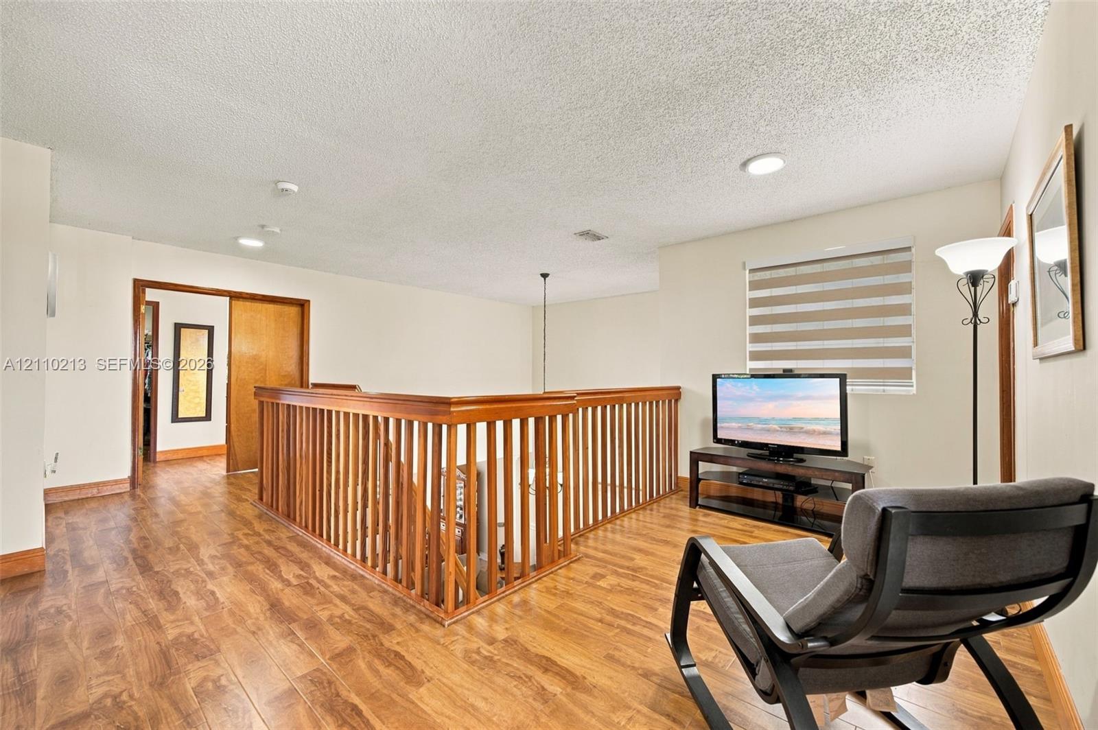 Wood-finish flooring, custom wooden staircase railing, recessed lighting, and dual-layered window shades