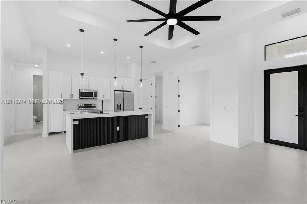Kitchen featuring a center island with slat detailing and a solid-surface countertop, white cabinetry, integrated stainless steel appliances, large-format tile flooring, and a coffered ceiling with a multi-blade ceiling fan