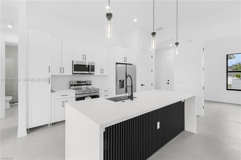 Kitchen featuring white cabinetry, quartz countertops, a black slatted-detail island with an undermount sink, matte black faucet, and three glass pendant lights