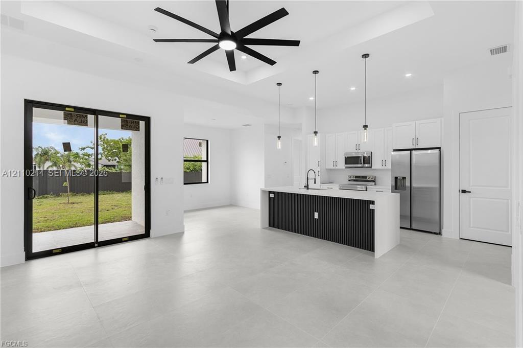 Open-concept area featuring a coffered ceiling with a black multi-blade ceiling fan, large-format tile flooring, a kitchen island with a slatted base and quartz-finish countertop, stainless steel appliances, and sliding glass doors