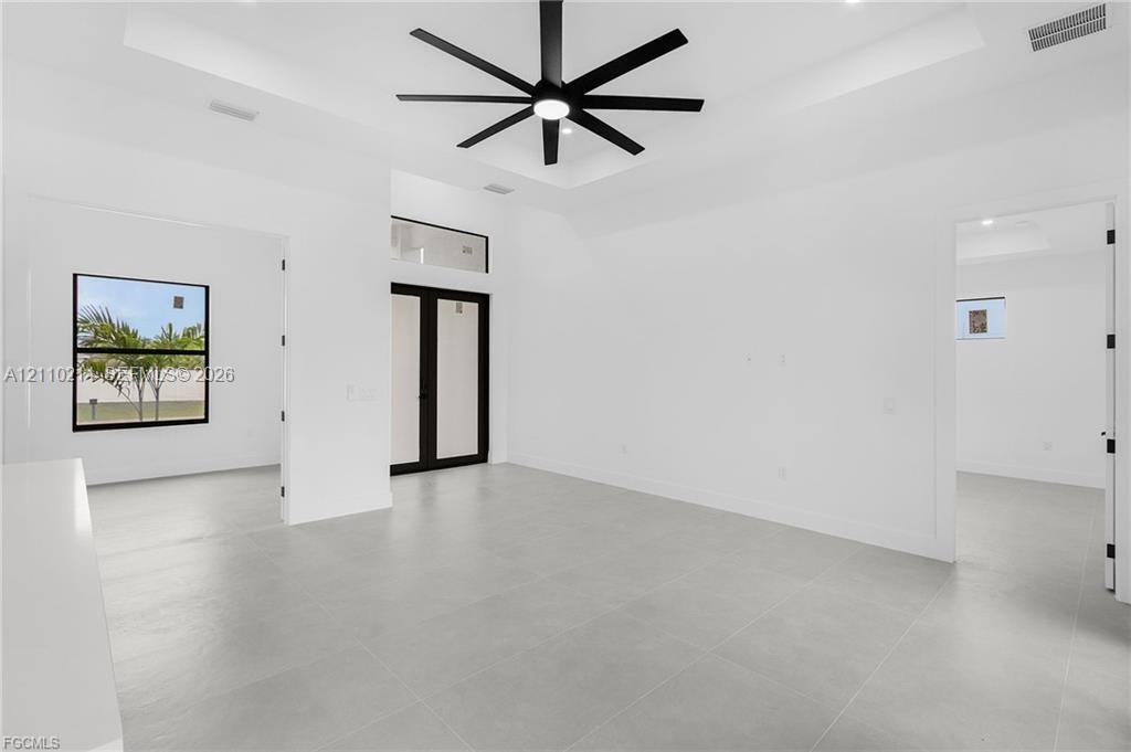 Tray ceiling, large-format tile flooring, matte black multi-blade ceiling fan, and black-framed glass entry doors with transom window