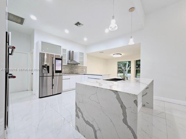Kitchen featuring a waterfall-edge island with stone-finish countertops, stainless steel appliances, white cabinetry with glass-panel uppers, tile backsplash, and large-format porcelain tile flooring