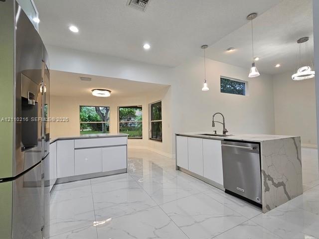 Kitchen featuring high-gloss white cabinetry, large-format tile flooring, a stone-surface island with waterfall edge, stainless steel appliances, and recessed and pendant lighting