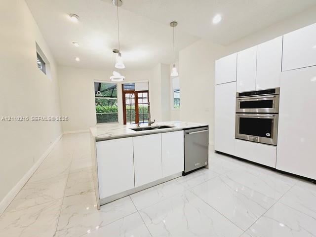 Modern kitchen featuring floor-to-ceiling white cabinetry, stone-finish countertops, stainless steel double wall ovens, a central island with an integrated sink, and large-format porcelain tile flooring