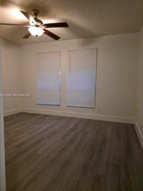 Interior space featuring wood-finish flooring, neutral wall paint, and a ceiling fan with integrated lighting, complemented by dual windows with installed blinds