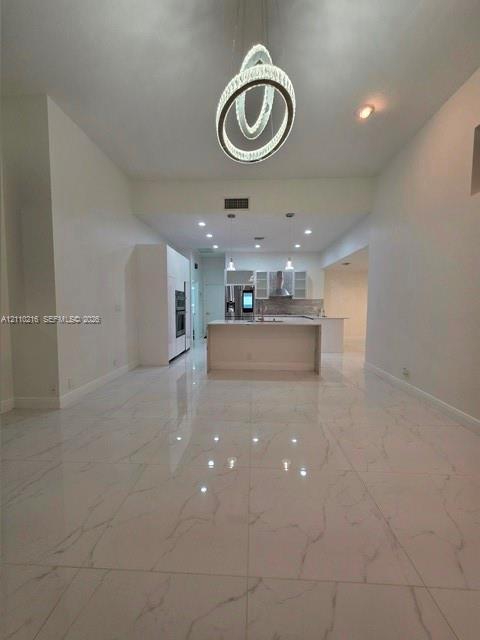 Large-format porcelain tile flooring with veining detail, central island with waterfall edge, recessed ceiling lighting, and sculptural multi-ring pendant fixture