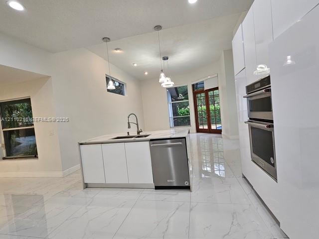 Modern kitchen featuring high-gloss white cabinetry, a center island with a stone-finish countertop, stainless steel double wall ovens, a stainless steel dishwasher, and polished tile flooring