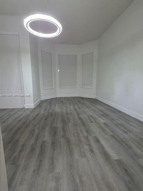 Interior space featuring wood-finish flooring, a contemporary circular LED chandelier, three bay windows, and neutral wall tones