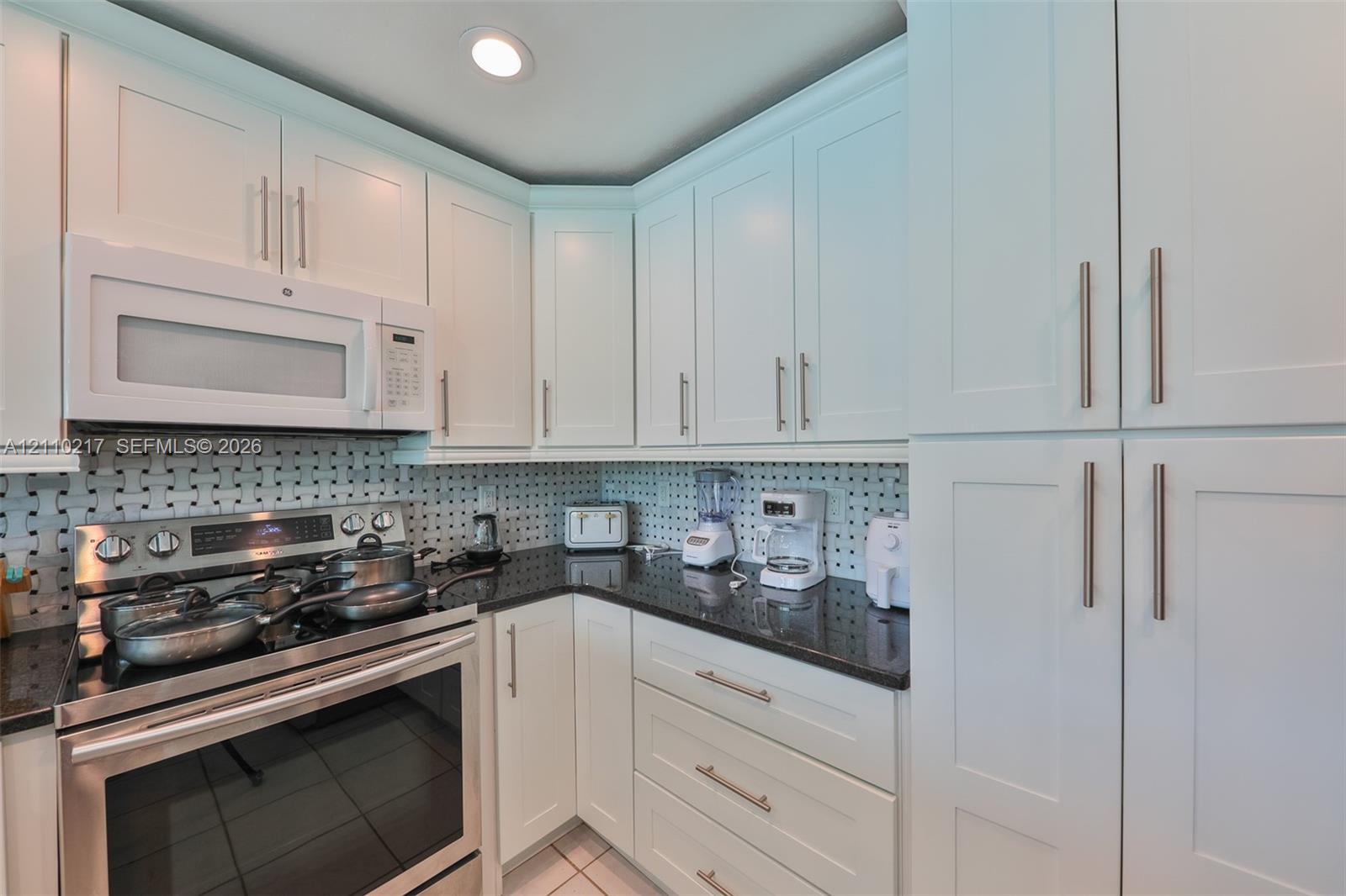 Kitchen featuring white shaker-style cabinetry, dark stone countertops, stainless steel appliances, and a geometric tile backsplash