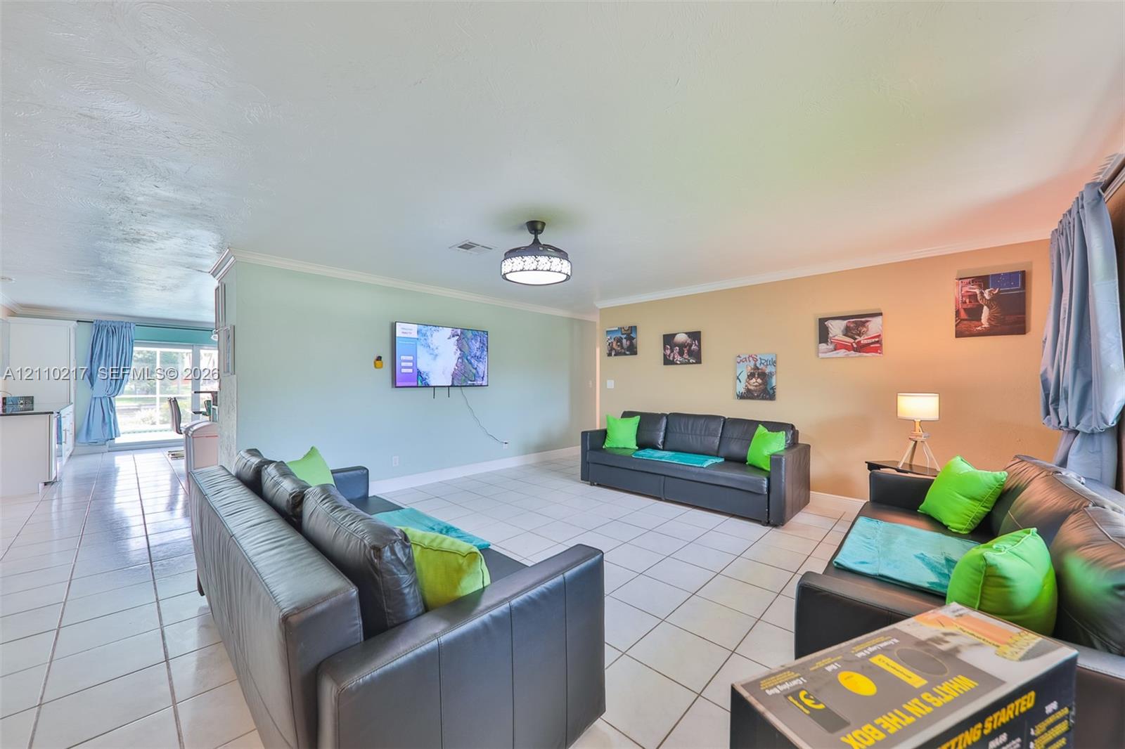 Open-concept interior featuring light-colored tile flooring, a central ceiling fan with integrated lighting, and crown molding