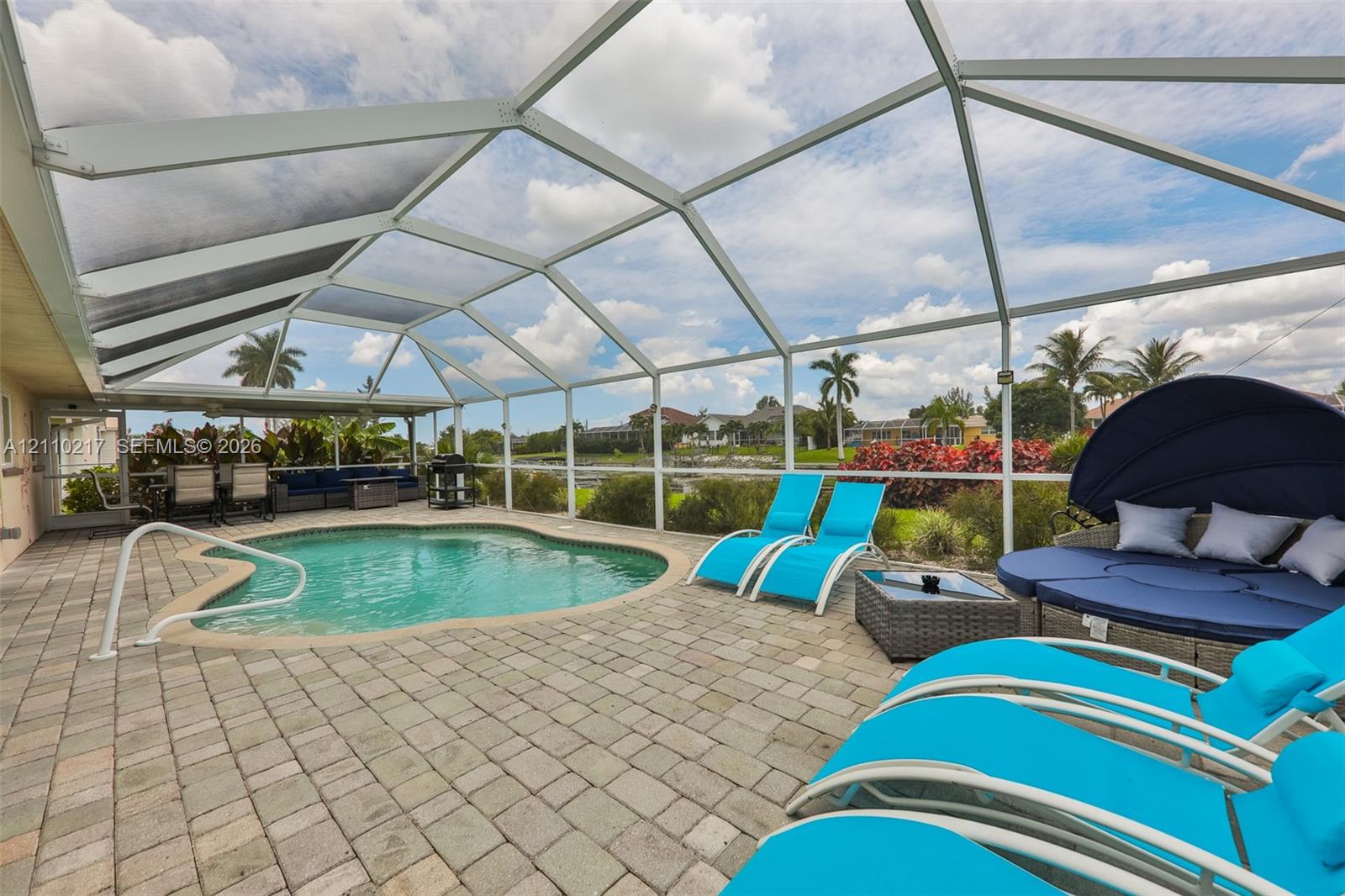 Screened-in patio featuring a concrete paver deck, a kidney-shaped pool, and an integrated handrail