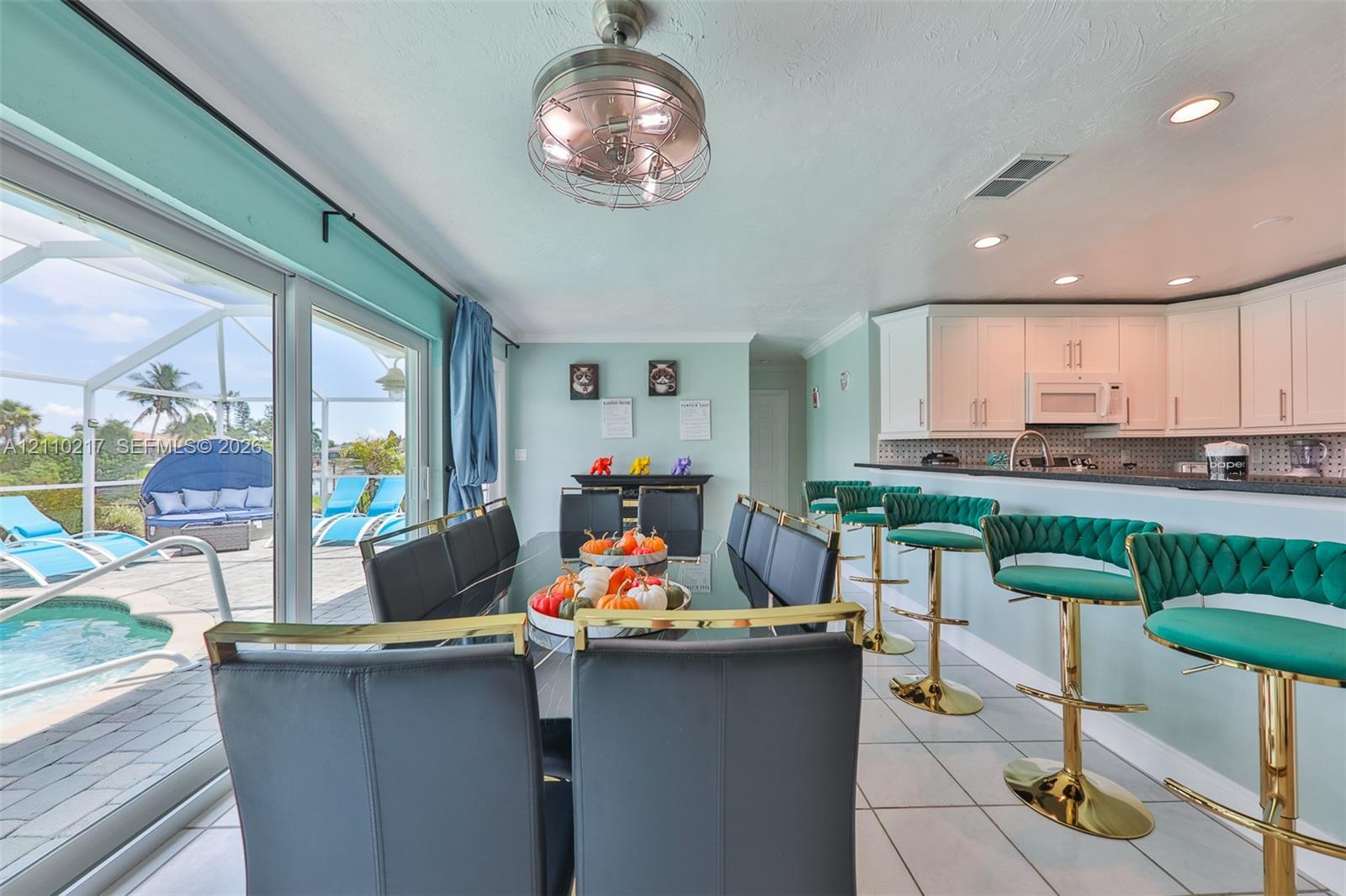 Open-concept kitchen and dining area featuring white shaker-style cabinetry, dark stone countertops, recessed lighting, and expansive sliding glass doors leading to a screened lanai with a swimming pool
