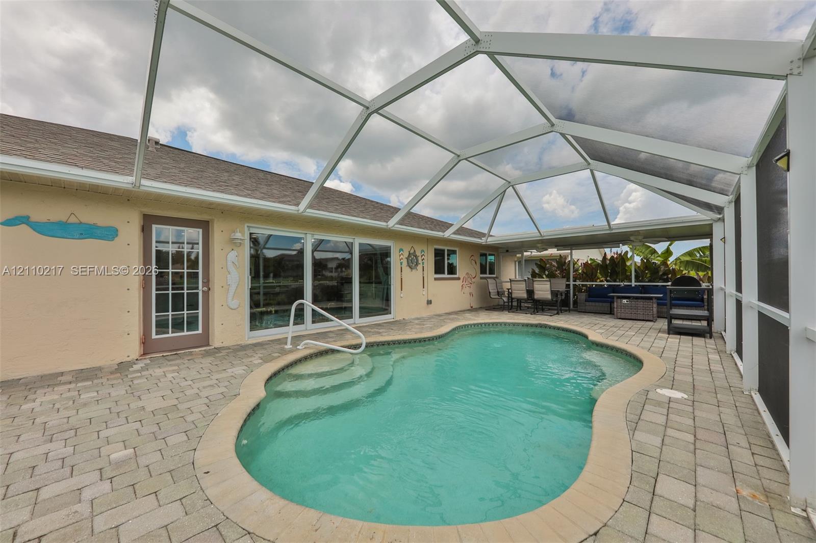 Screen-enclosed patio featuring a paver deck and a custom-shaped swimming pool with built-in steps and a metal handrail