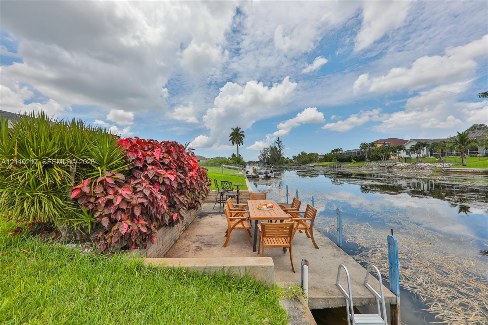 Waterfront concrete dock featuring a built-in swimming ladder, stone retaining wall, and mature tropical landscaping