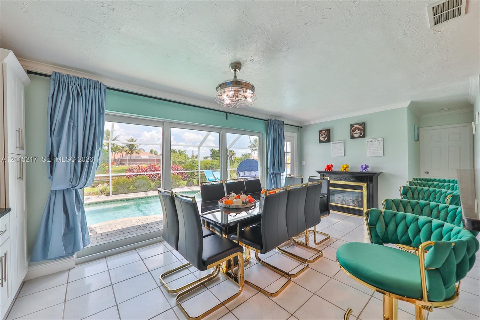 Open-concept dining area featuring large sliding glass doors, white ceramic tile flooring, a mounted electric fireplace with a black surround, and a central ceiling fan with integrated lighting