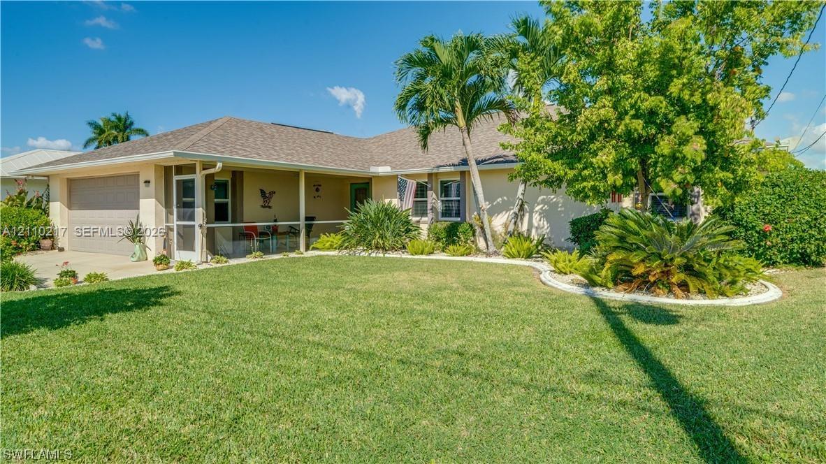 Single-story residence featuring a covered front entryway, attached two-car garage, and asphalt shingle roofing, complemented by established palm trees and manicured landscape curbing