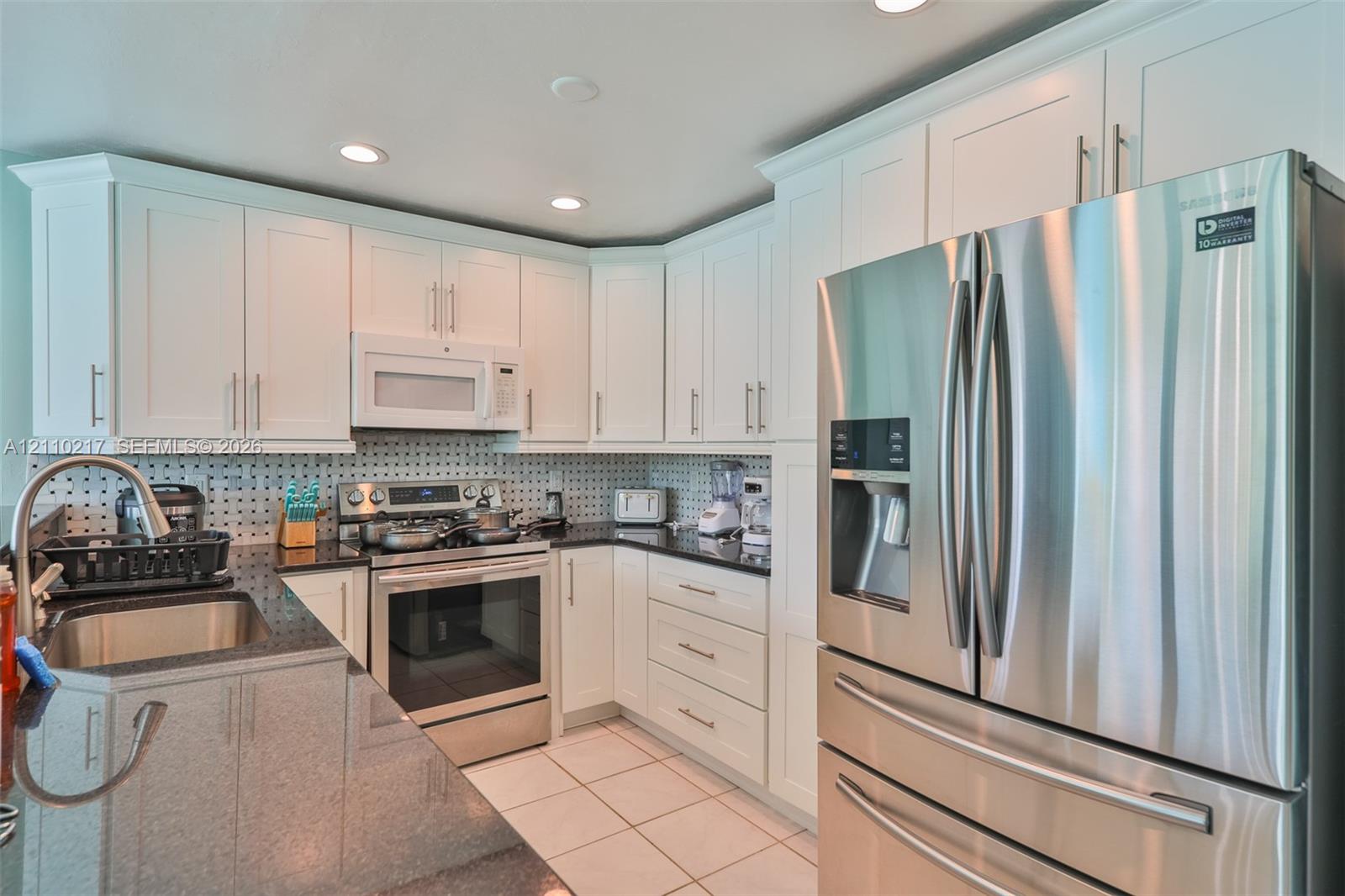 Kitchen featuring white shaker-style cabinetry, dark stone countertops, stainless steel appliances, a mosaic-tiled backsplash, and recessed ceiling lighting