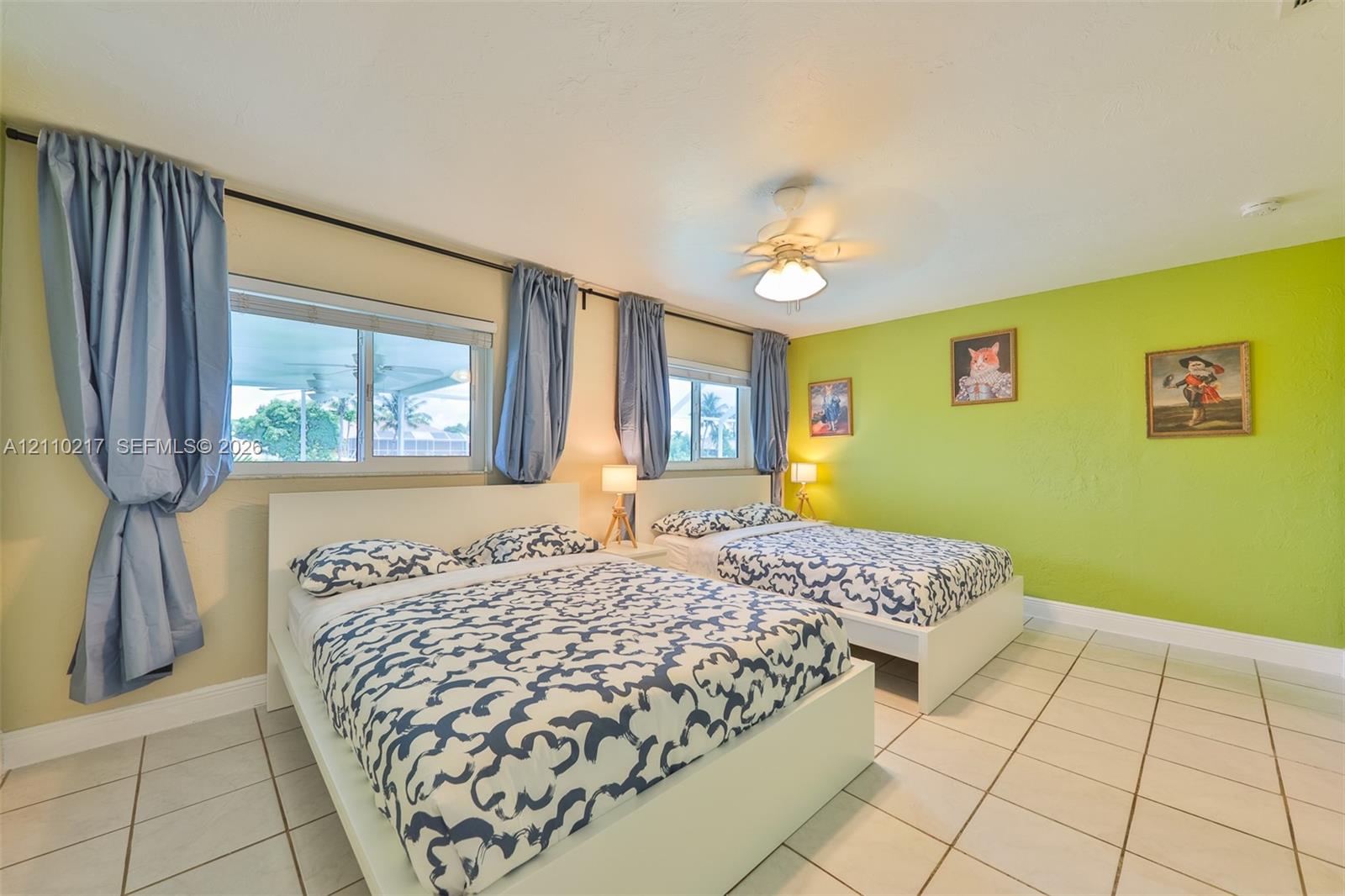 Spacious interior featuring large-format tile flooring, dual sliding windows with natural lighting, and a white ceiling fan with integrated light fixture