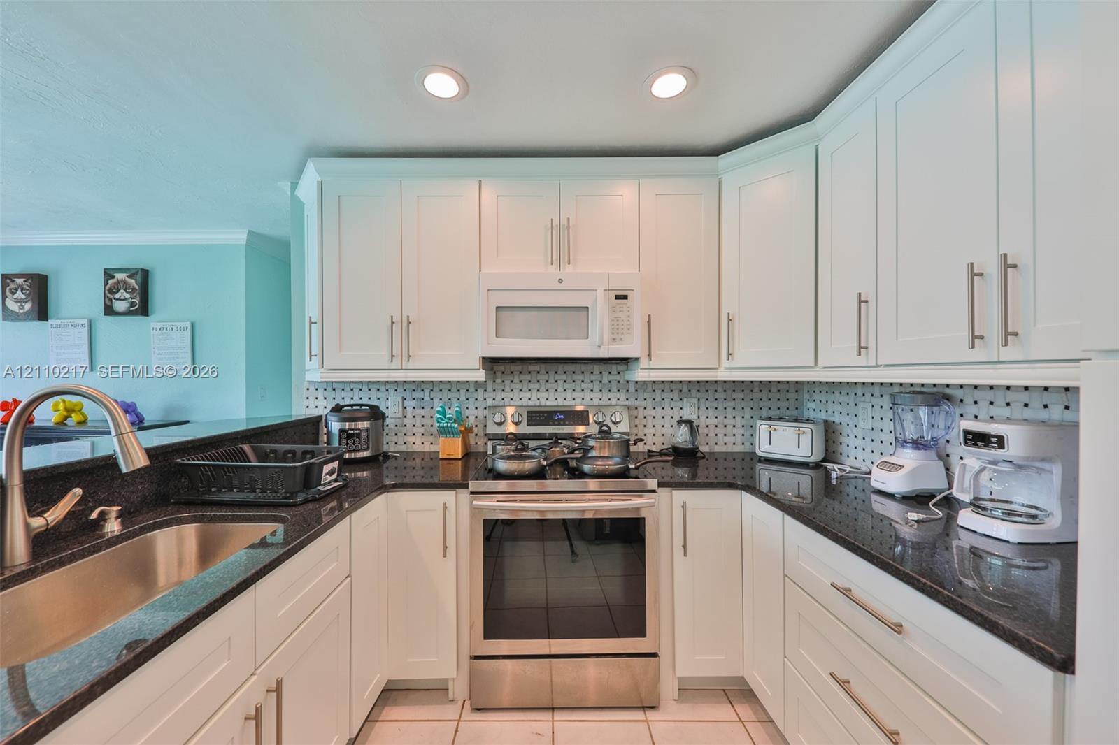 Kitchen featuring white shaker-style cabinetry, dark stone countertops, stainless steel appliances, a tile backsplash, and recessed lighting
