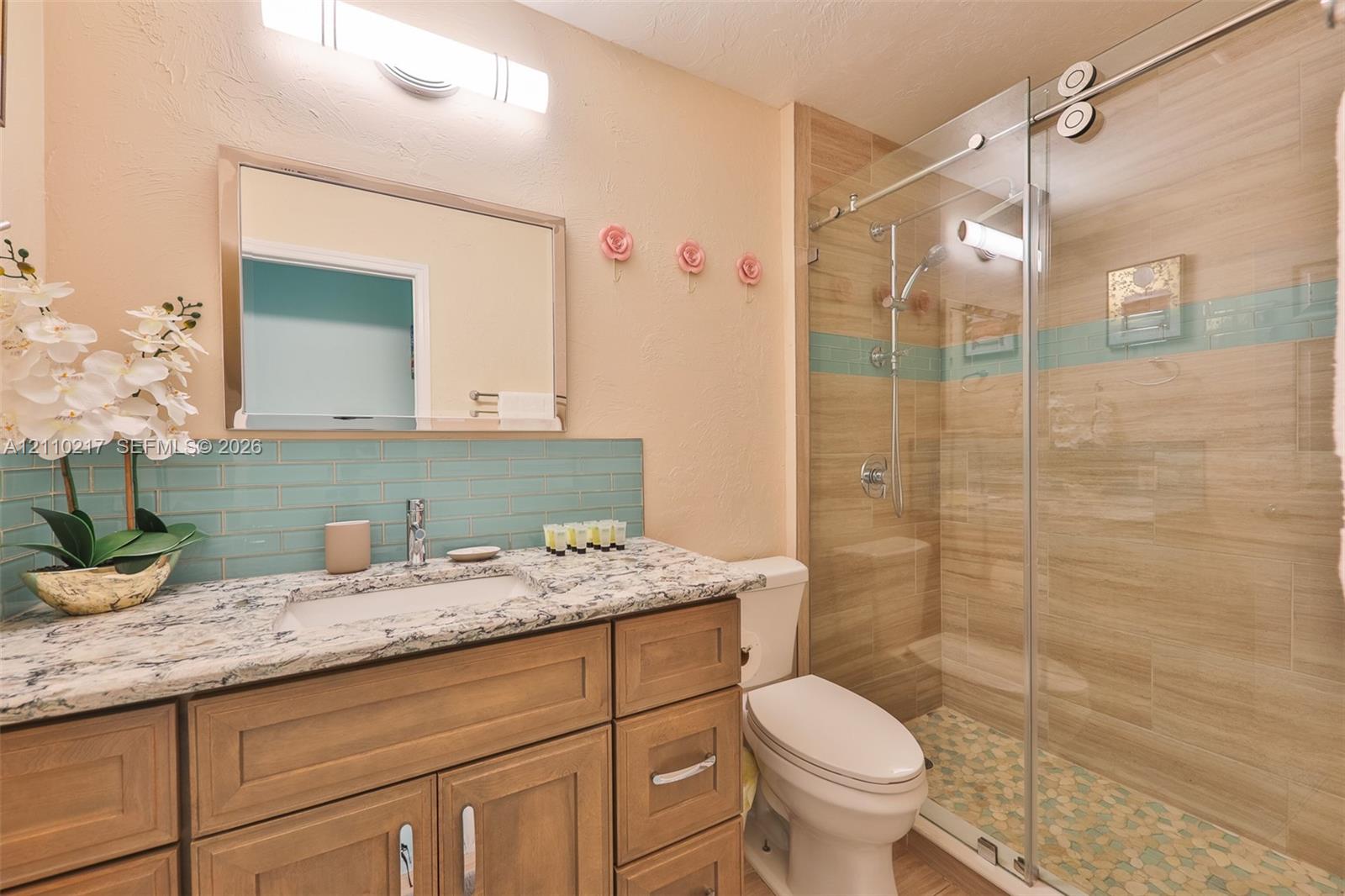 Bathroom vanity featuring a stone-look countertop, undermount sink, blue subway tile backsplash, and wood-finish cabinetry