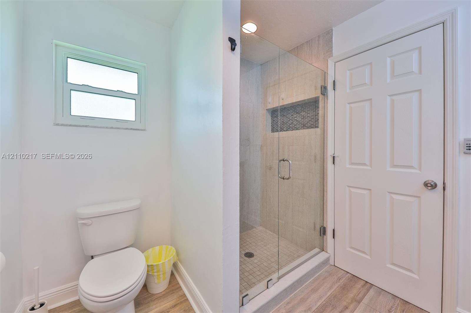 Bathroom featuring a glass-enclosed shower with tiled surround and built-in niche, wood-finish flooring, and a six-panel door