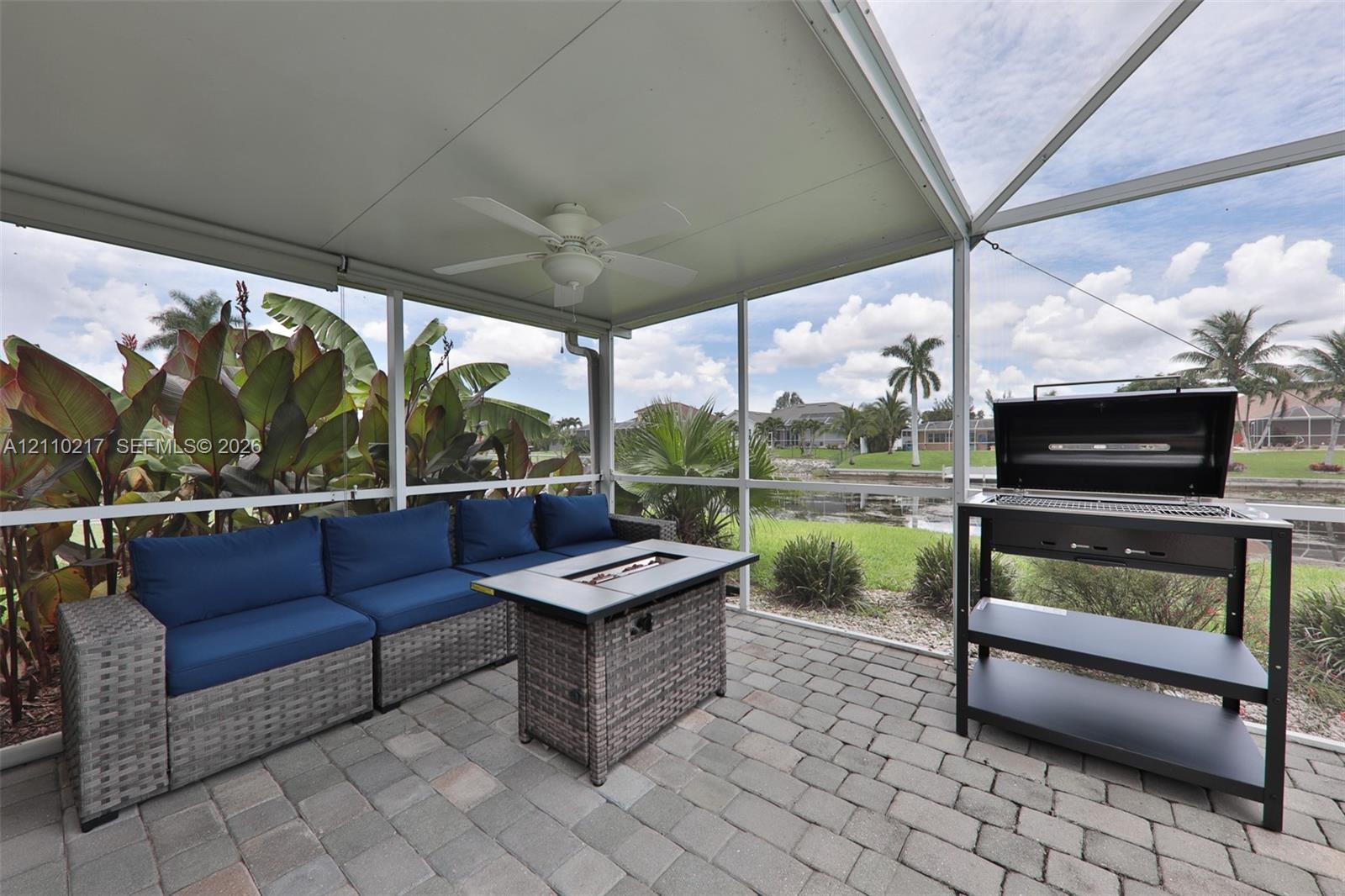 Screened-in lanai featuring a paver floor, overhead ceiling fan, and metal grill station
