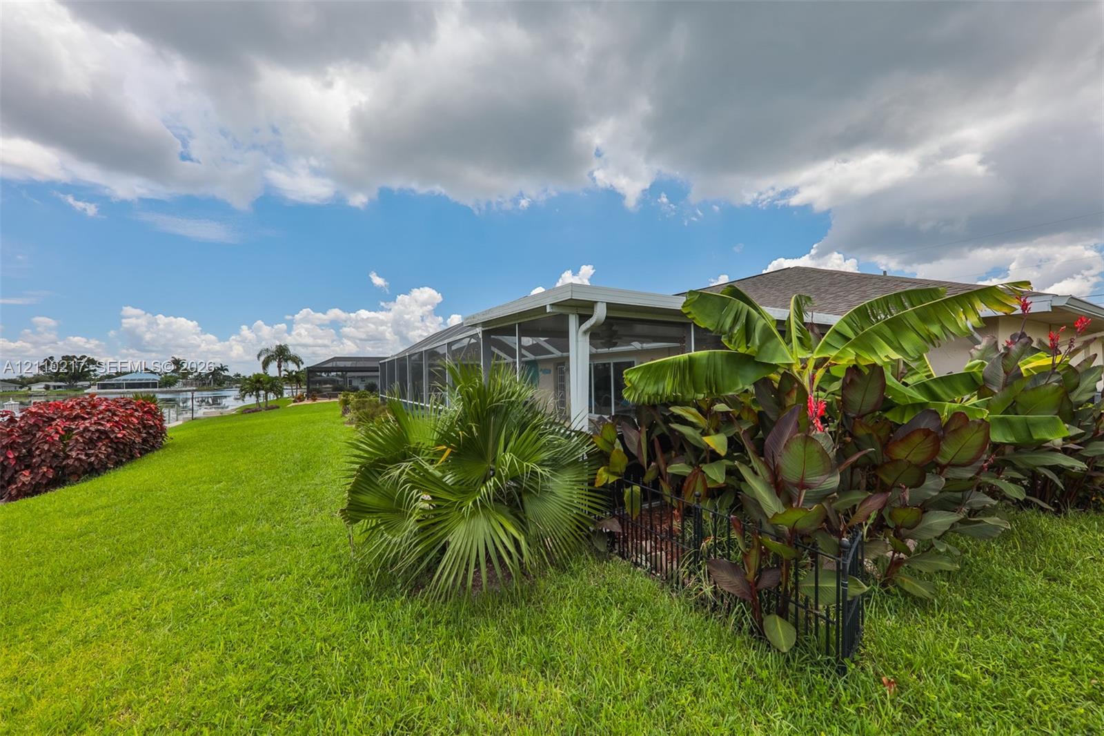 Screened-in lanai featuring a manicured lawn, established tropical landscaping, and water frontage