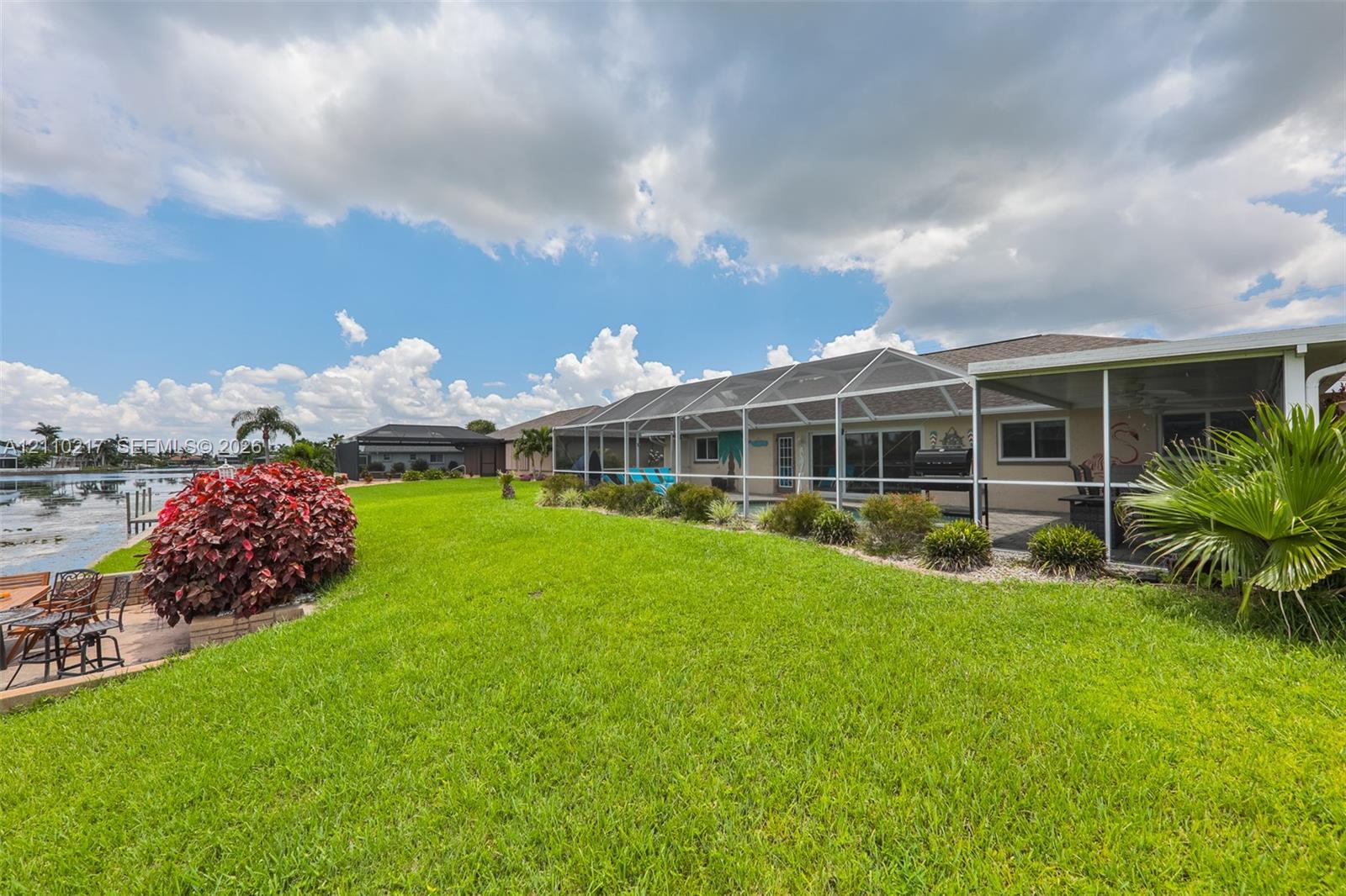 Rear exterior featuring a screened-in lanai, manicured lawn, water frontage, and native landscaping