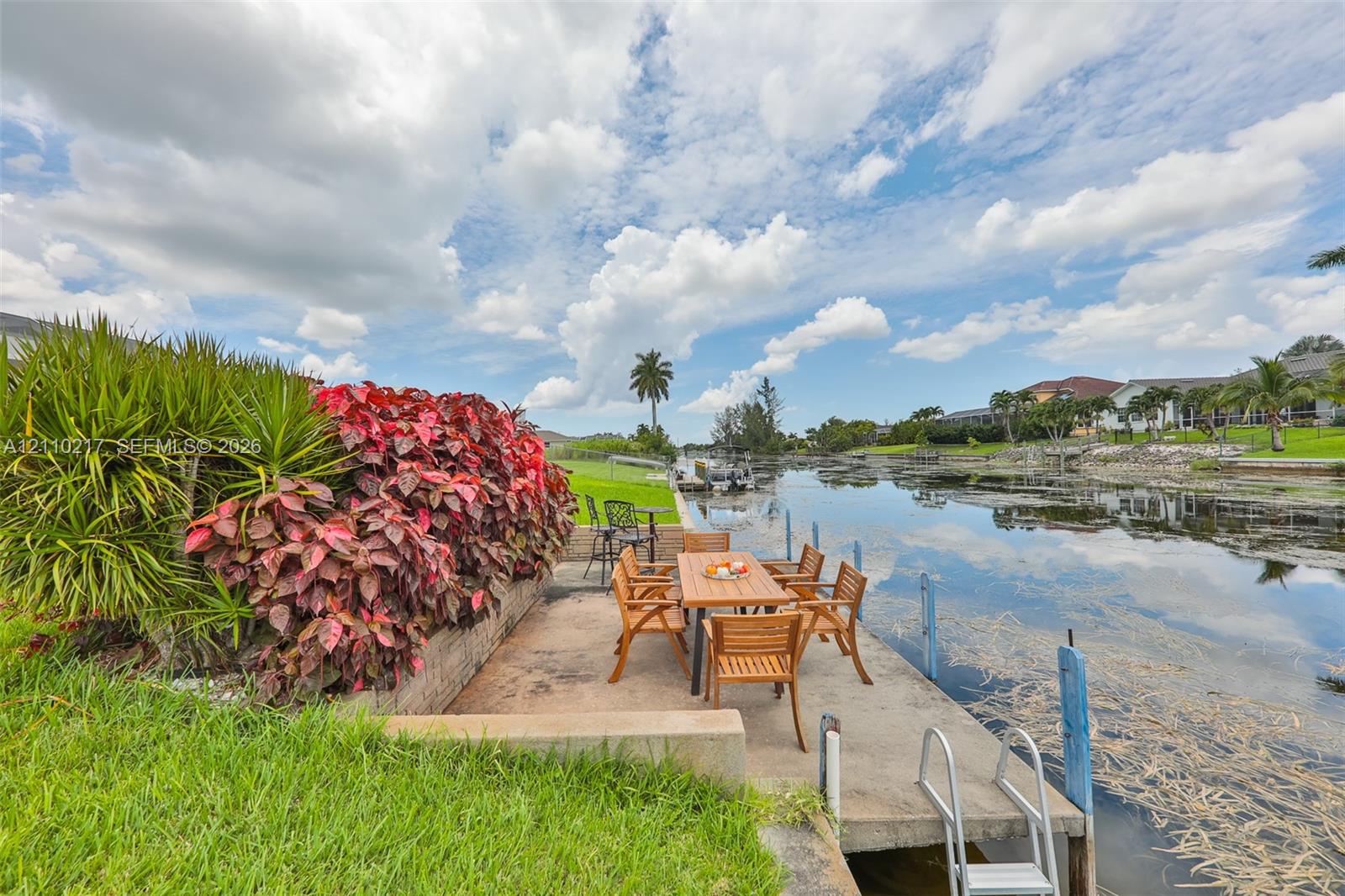 Concrete waterfront dock featuring a built-in ladder, canal bulkhead, and integrated landscaping with mature foliage