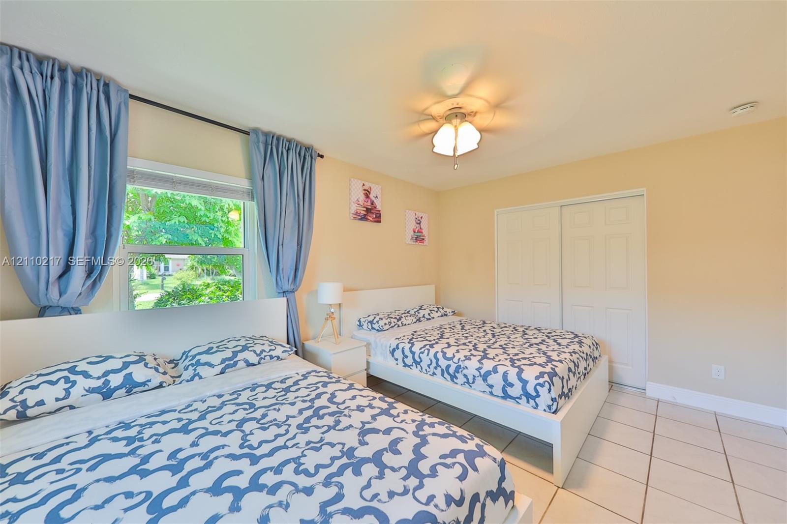 Room featuring neutral wall paint, tile flooring, sliding closet doors, and a ceiling fan with light fixture