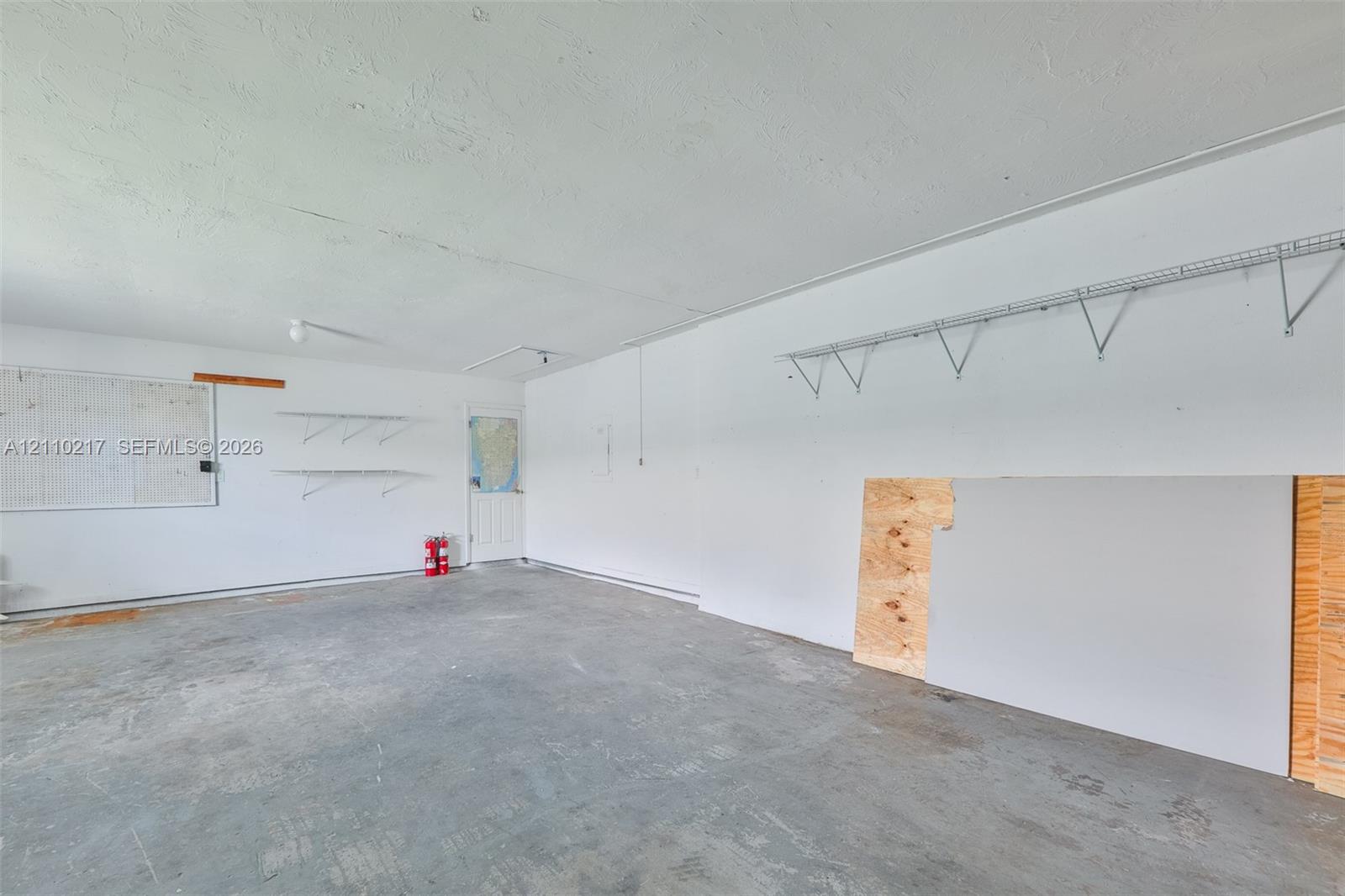 Garage interior featuring finished walls, concrete flooring, and installed wire shelving units