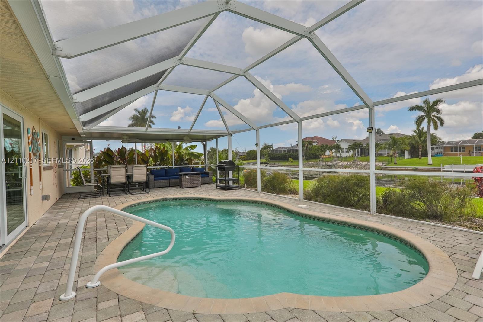 Screened-in patio area featuring a paver deck, inground swimming pool with a metal handrail, and a covered lanai