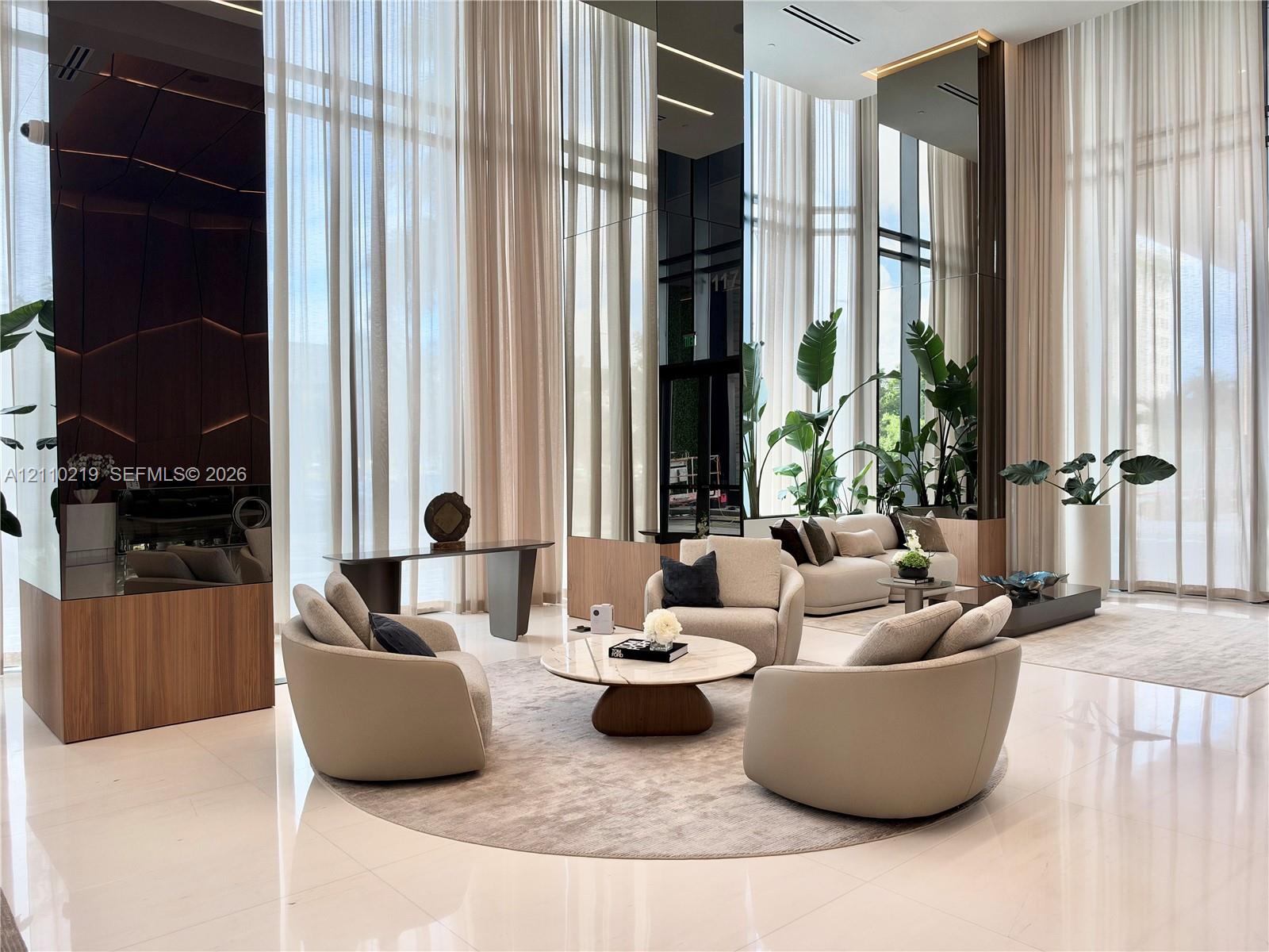 Double-height floor-to-ceiling windows, polished stone flooring, integrated linear lighting, mirrored wall accents, and wood-finish paneling