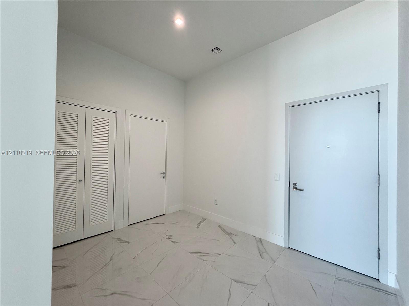 High-ceiling entryway featuring large-format tile flooring with marble-pattern veining, recessed lighting, and white louvered closet doors