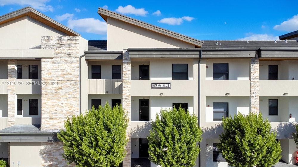 Contemporary multi-level exterior featuring stacked stone veneer accents, shed-style rooflines, smooth stucco finish, and private recessed balconies