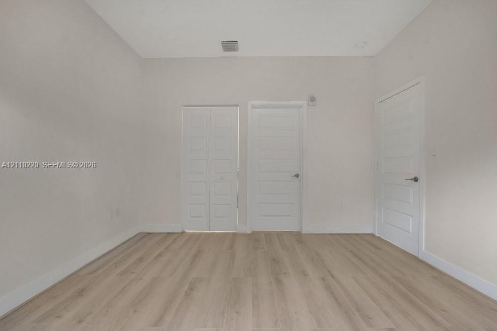 Room featuring light-toned wood-finish flooring, neutral walls, two five-panel interior doors, and one set of bifold closet doors with brushed nickel hardware