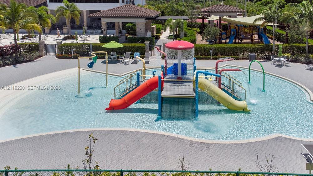 Splash pad featuring integrated water slides, overhead water features, zero-entry pool basin, and surrounding paved pool deck