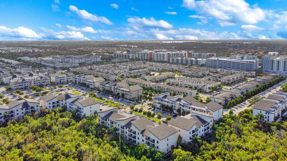 Aerial perspective of residential community featuring multi-story building clusters, shingled roofing, private balconies, and established perimeter vegetation