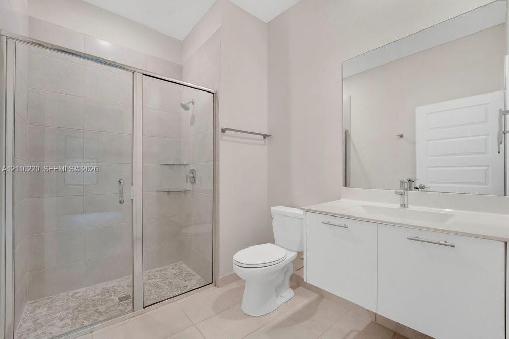 Bathroom featuring a glass-enclosed shower with tiled walls and flooring, a wall-to-wall vanity with an integrated sink, a large vanity mirror, and a chrome-finish faucet