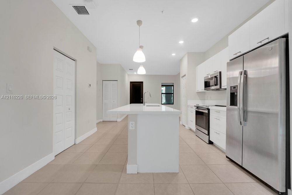 Kitchen featuring a central island with a solid-surface countertop, white flat-panel cabinetry, stainless steel appliances, recessed ceiling lighting, and large-format tile flooring