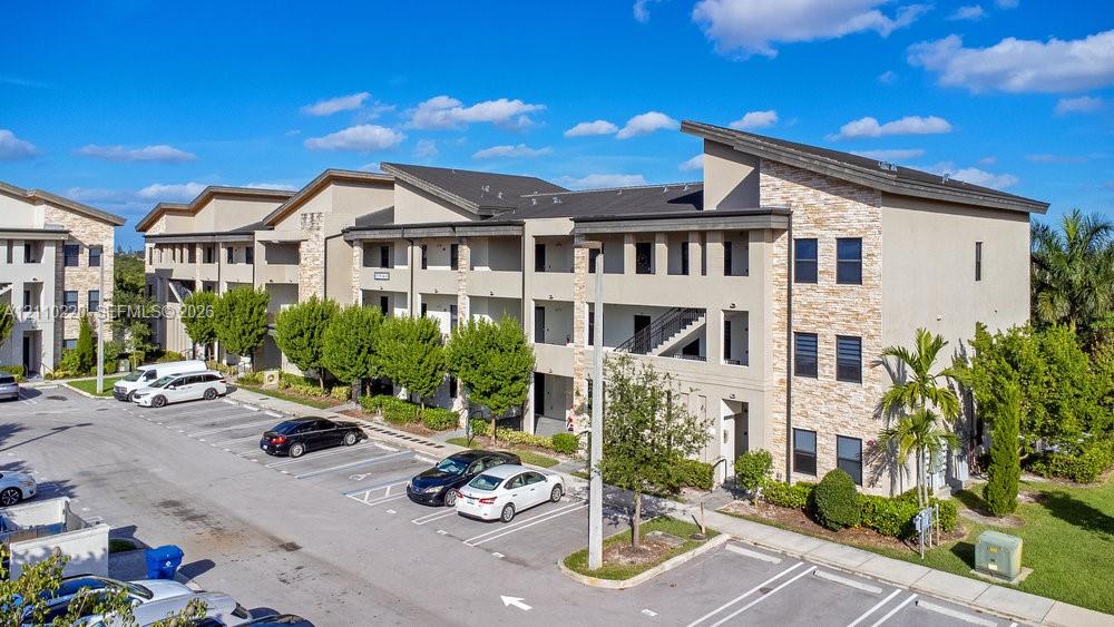 Multi-story residential complex featuring stucco exterior walls, stone veneer accents, shed-style rooflines, and dedicated surface parking