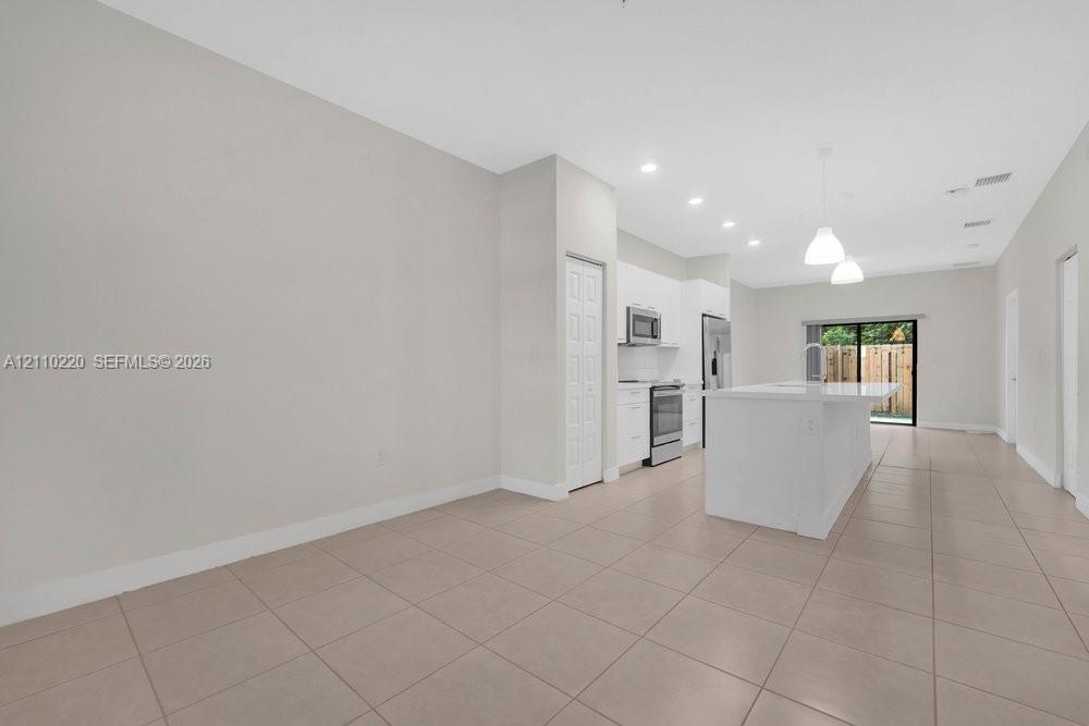 Open-concept kitchen featuring a center island with countertop seating, white cabinetry, stainless steel appliances, tile flooring, and recessed lighting