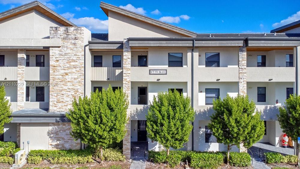 Modern multi-story exterior featuring light-colored stucco, natural stone accents, shed rooflines, and private covered balconies
