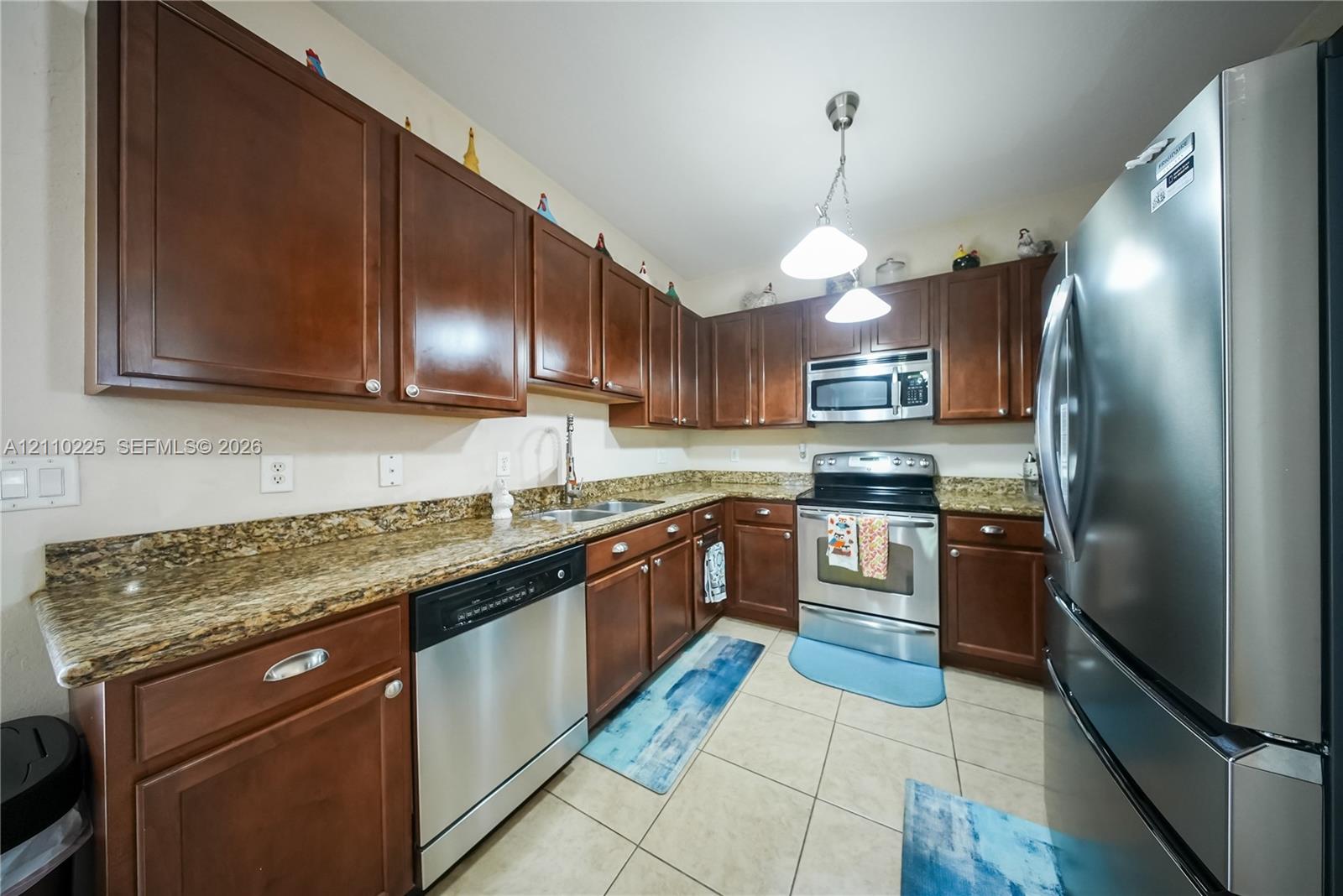 Kitchen featuring stained wood cabinetry, stone-finish countertops, stainless steel appliances, and large-format tile flooring